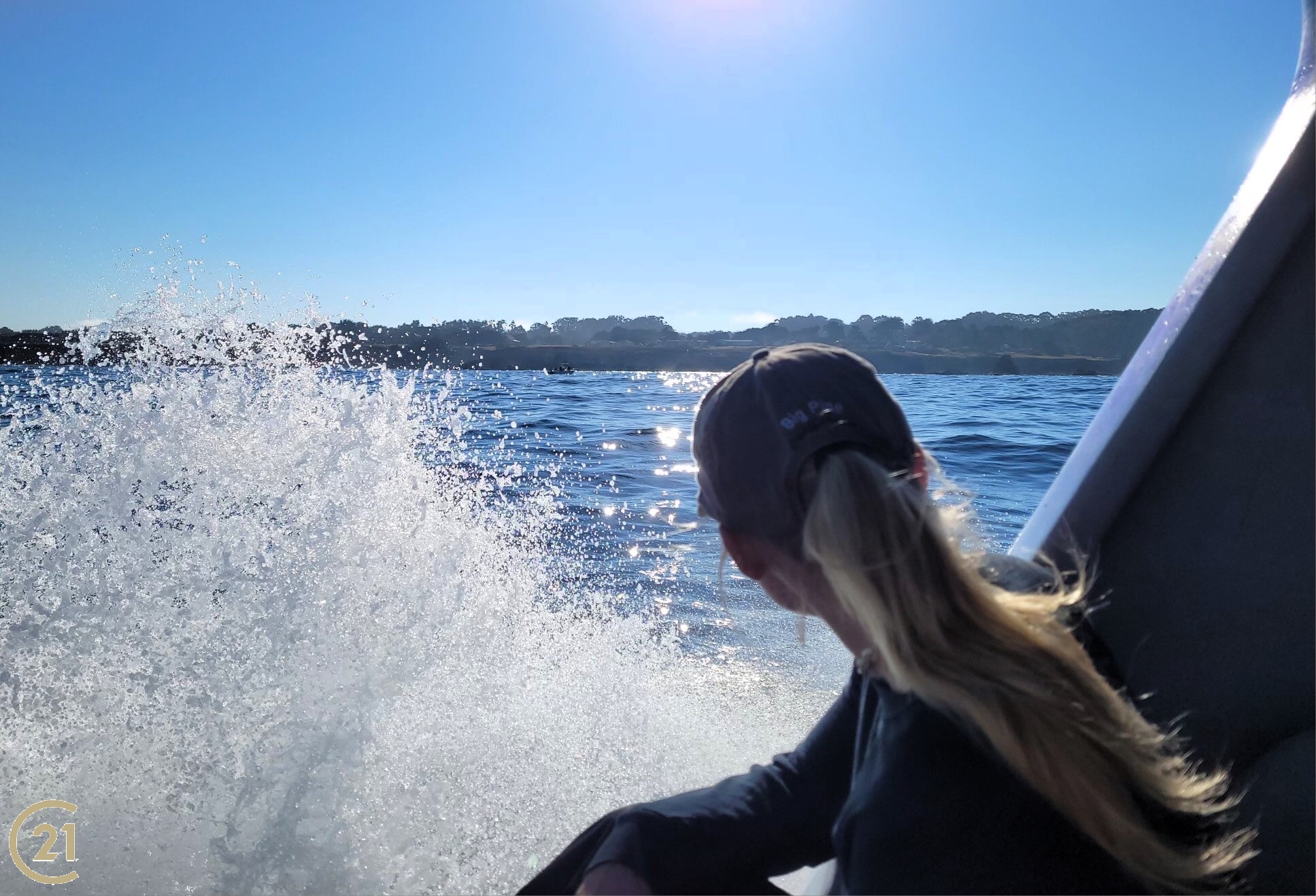 Girl on boat with ocean spray, looking back at coastline